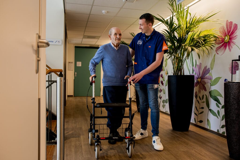 Cliënt en zorgmedewerker lopen samen over de gang